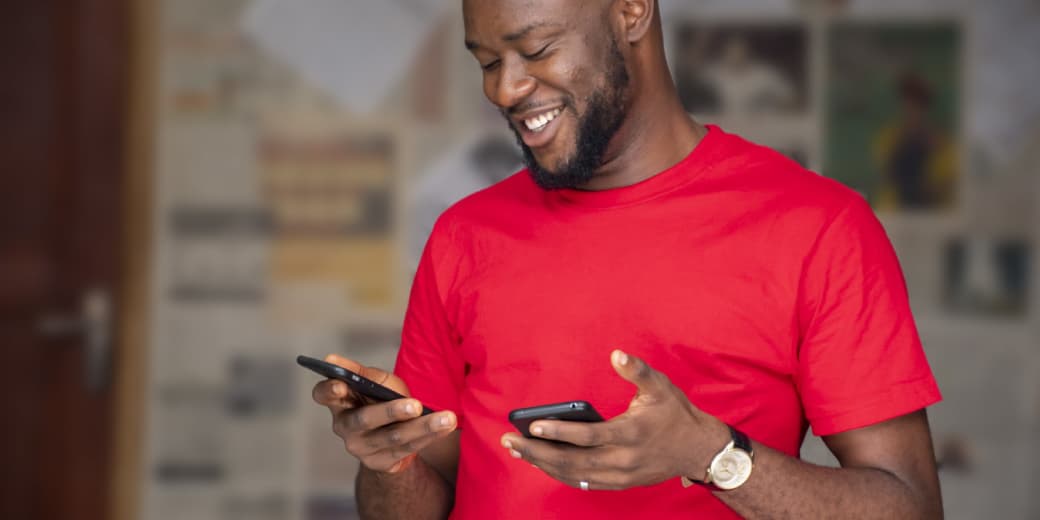 A smiling man using two smartphones. Credit: Wirestock | magnific.com.