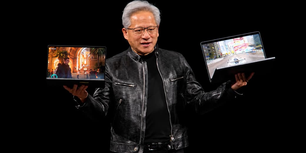NVIDIA CEO Jensen Huang holding two laptops on stage.