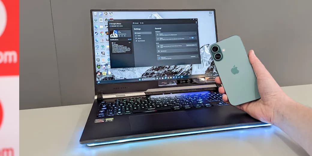 An iPhone held beside a Windows laptop displaying Phone Link settings.